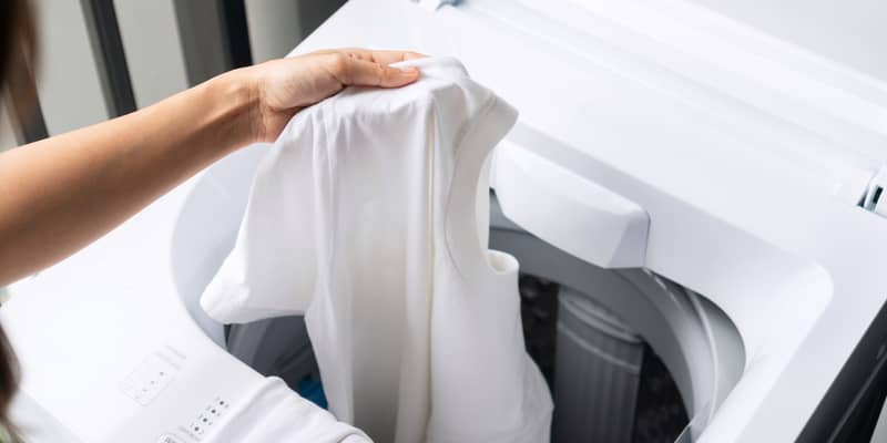 woman putting white color clothes into washing machine