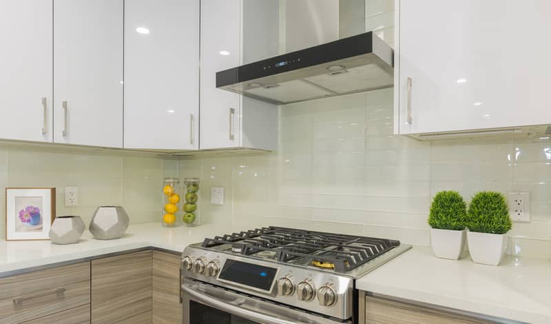 Modern kitchen interior with gas range, stainless steel fridge, white marble countertop.