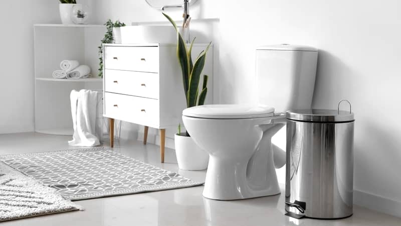 White toilet bowl and metallic trash bin in interior of light bathroom