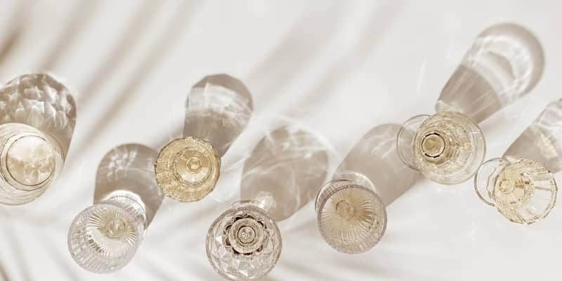 Top view white sparkling wine in different glasses of wine, stemmed glass with sun shadow palm leaf on light beige background.