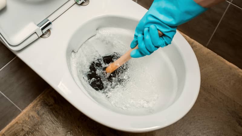 man's hand with blue gloves using plunger in toilet bowl