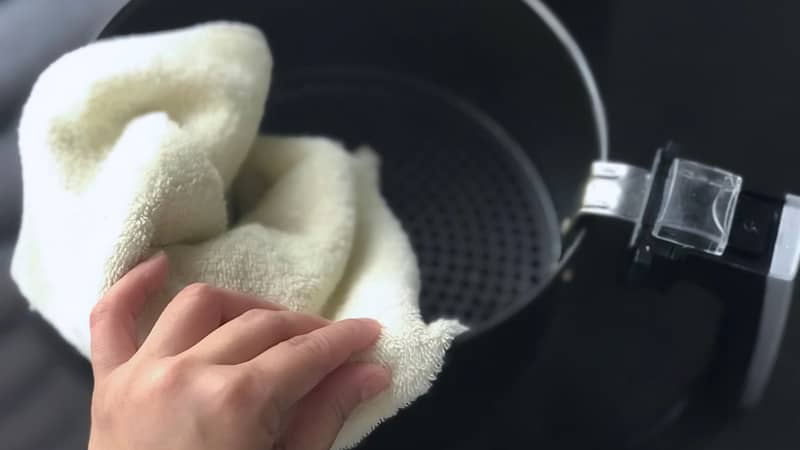 Women’s hand wipe the air fryer basket with kitchen towel.