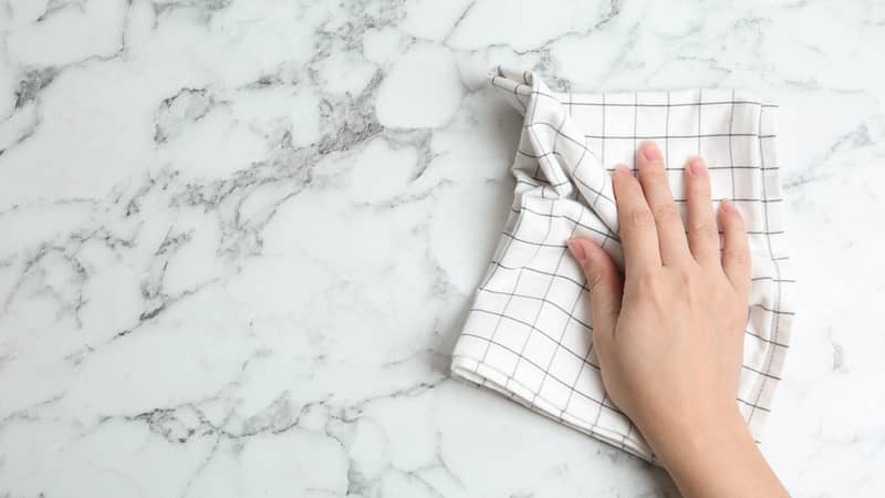 Woman wiping white marble table with kitchen towel