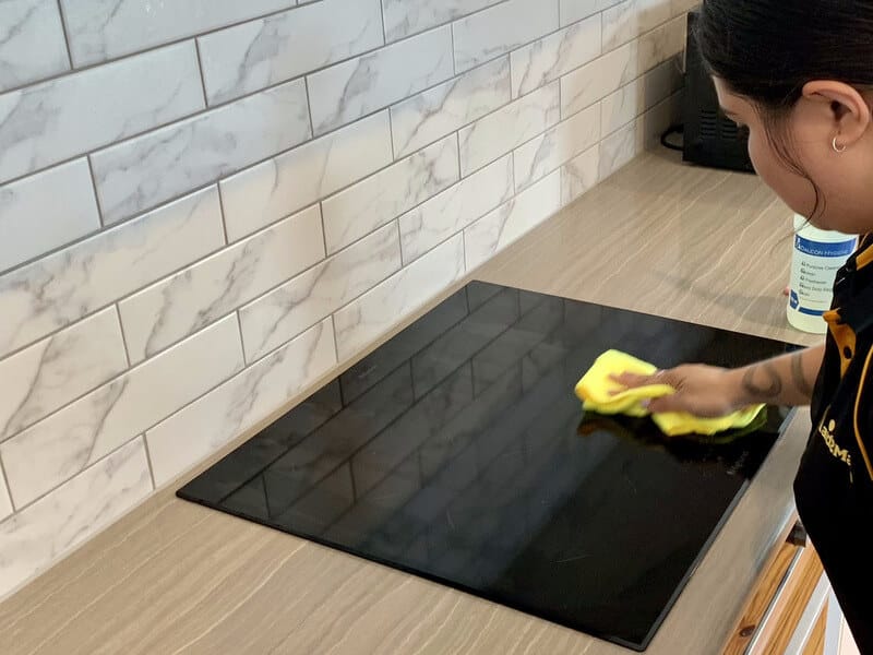 Professional cleaber wiping an induction cooktop with microfibre cloth