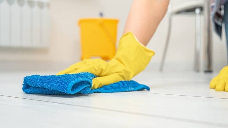 hands with yello gloves wiping tiled floor with blue terry cloth towel