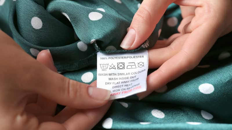 Woman reading clothing label with care instructions and content information on green polka dot polyester garment