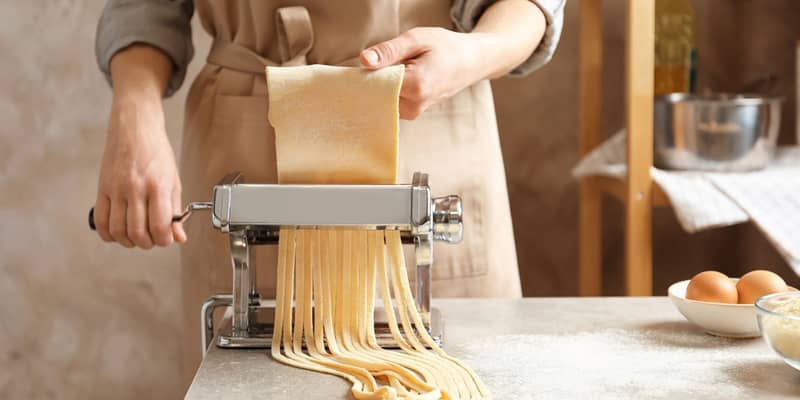 Young woman preparing noodles with pasta maker at table