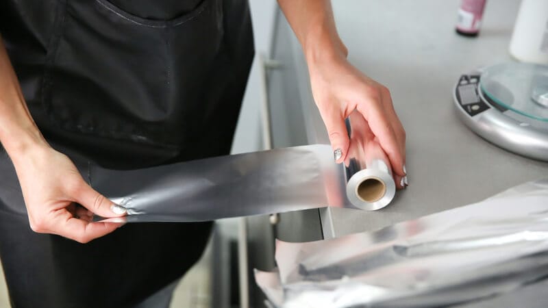 woman's hand unwinds a piece of aluminum foil from a roll