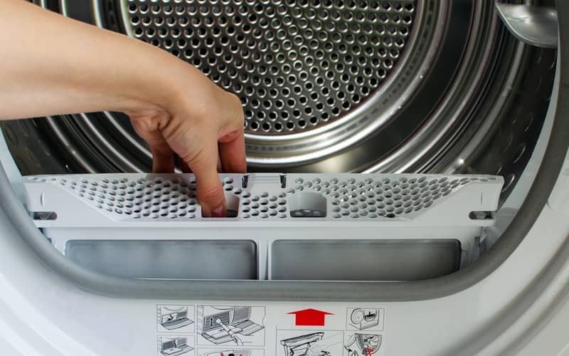 Hand holds a lint trap from a front-loading tumble dryer