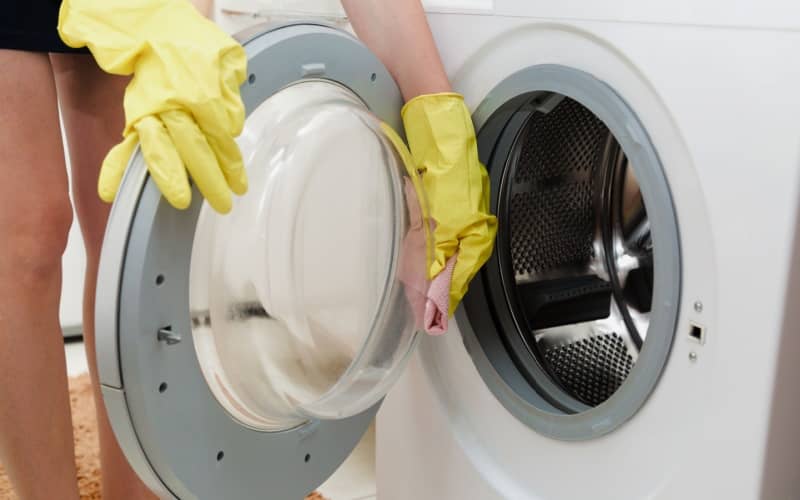 hands in yellow rubber gloves cleaning the glass of the washing machine door